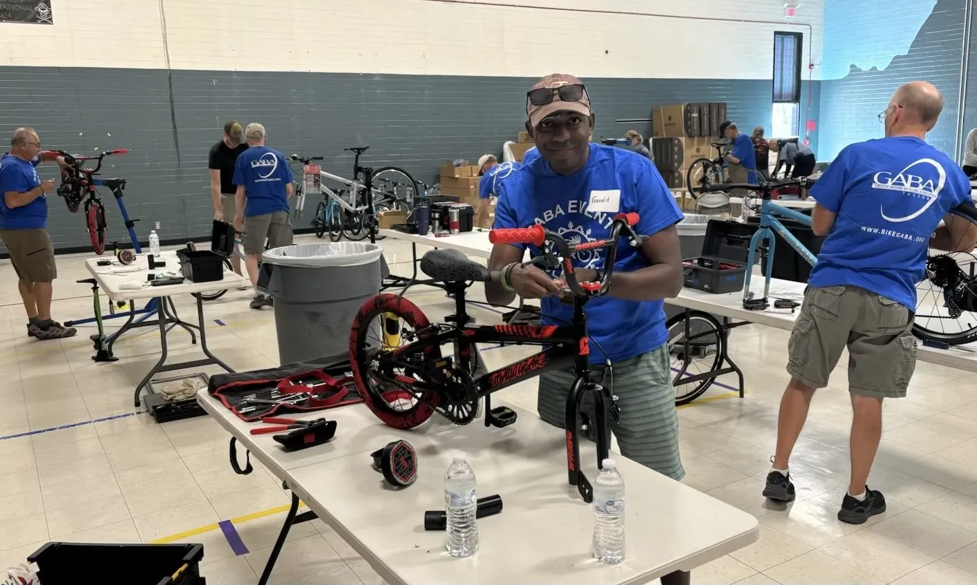 Volunteers in a gym assembling new childrens bikes on folding tables, one holding a finished red bike upright