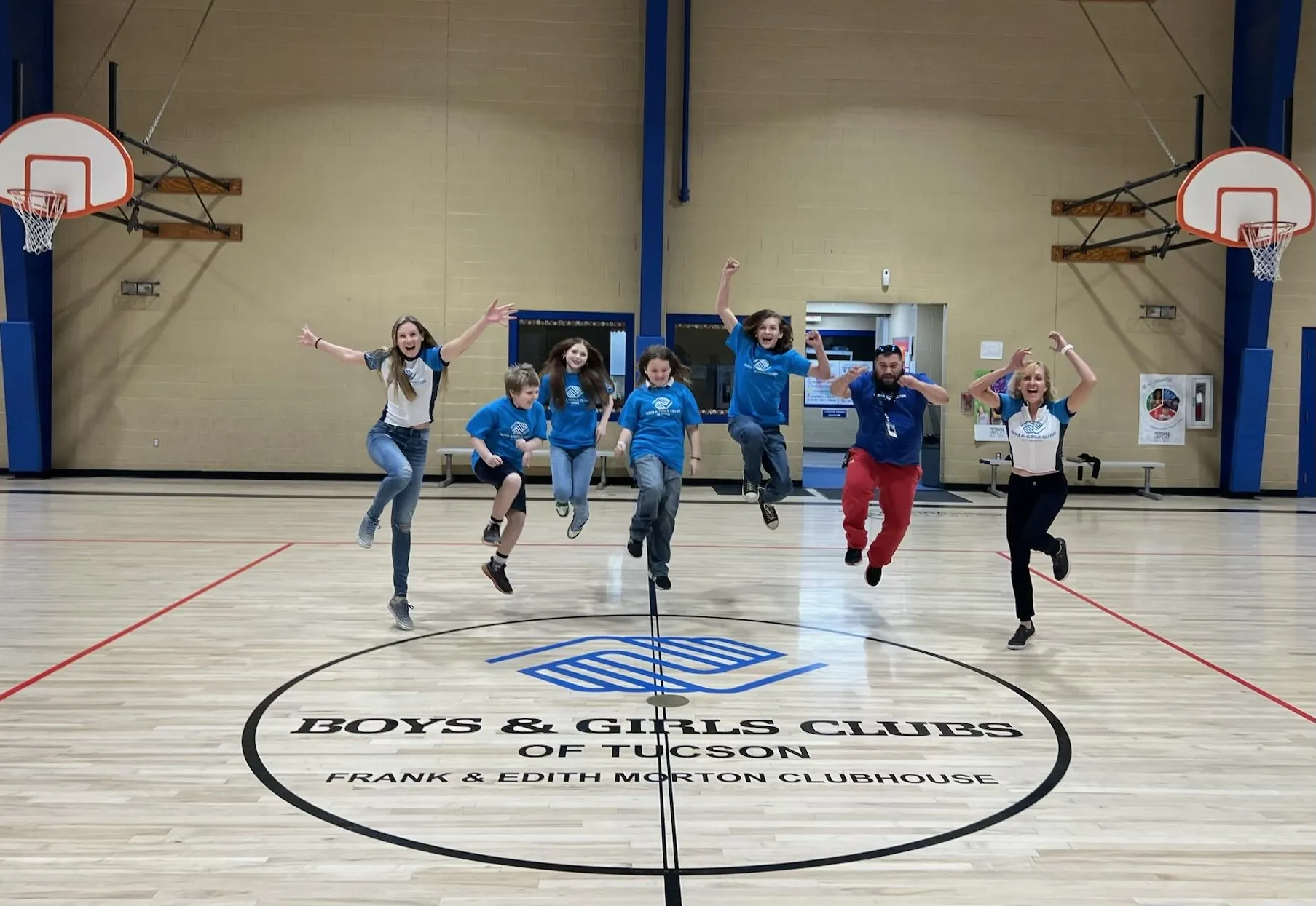 Six young riders and two adults from the Boys and Girls Clubs of Tucson jumping in the air together on a gym floor