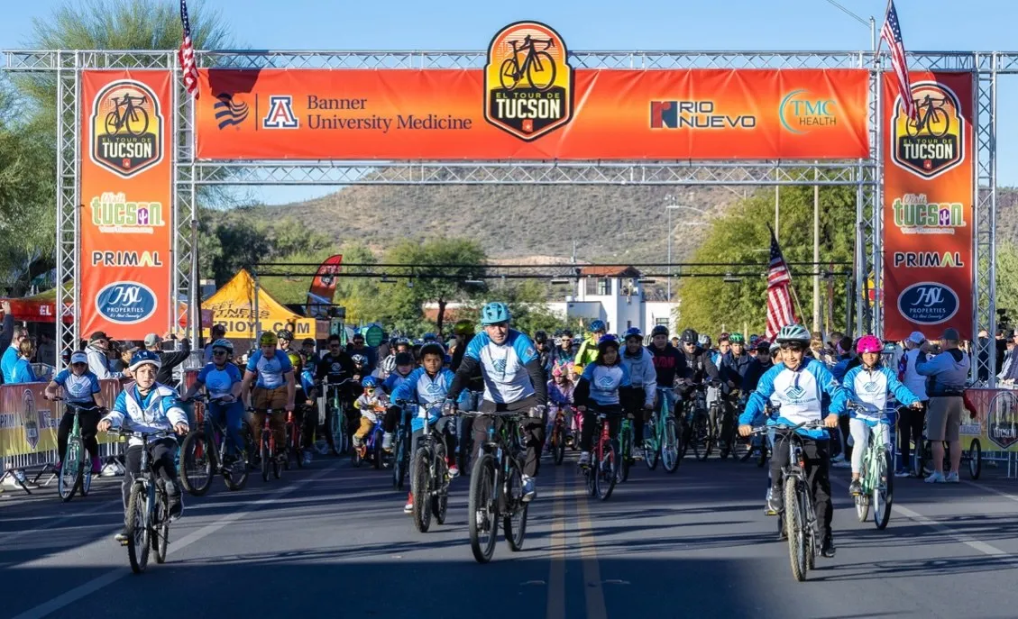 Young riders in club jerseys setting off under the El Tour de Tucson start arch